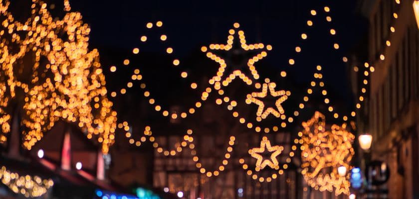 Illuminated holiday lights shaped like stars adorn a festive street.