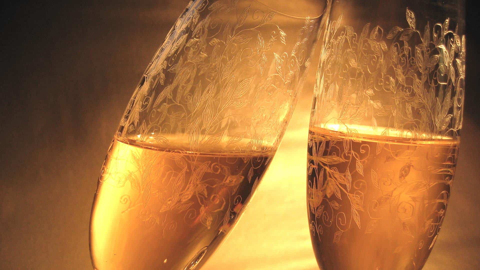Two intricately designed champagne flutes clinking together, filled with sparkling white wine.