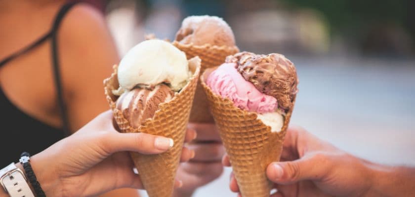Three hands holding ice cream cones with various flavors.