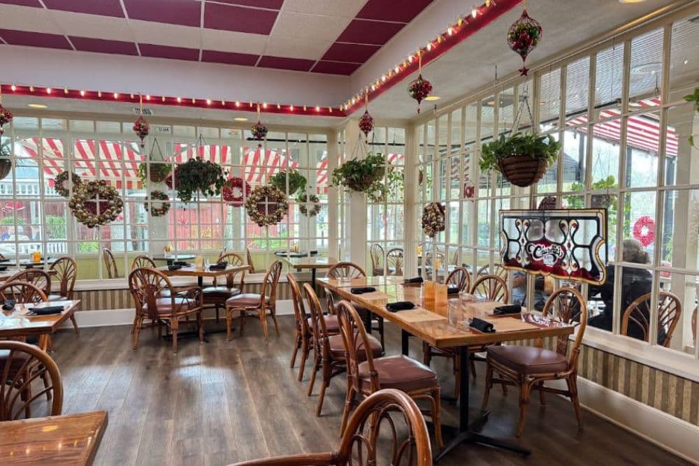 A cozy restaurant interior featuring wooden tables, wicker chairs, and festive decorations.