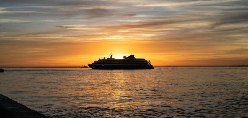 A silhouette of a cruise ship against a vibrant sunset over calm waters.