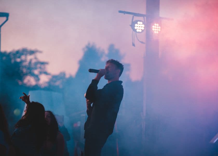 A singer performs on stage amidst colorful smoke at a live concert. A singer performs on stage amidst colorful smoke at a live concert.