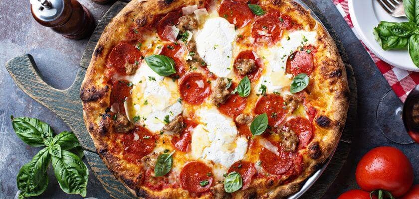 A delicious pepperoni pizza topped with mozzarella, basil, and sausage, served with fresh tomatoes and seasonings.