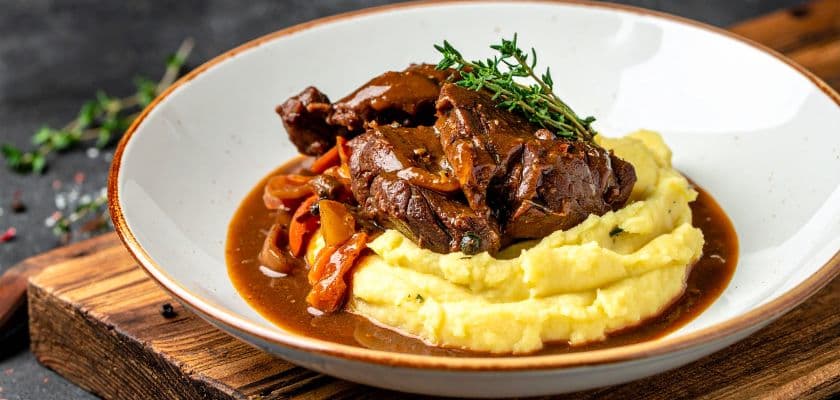 Birria braised short ribs with peppers and gravy are served over mashed potatoes.