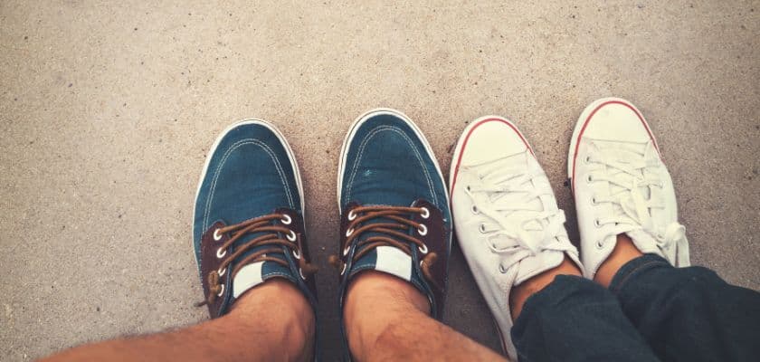 Two pairs of casual shoes side by side on sandy ground.