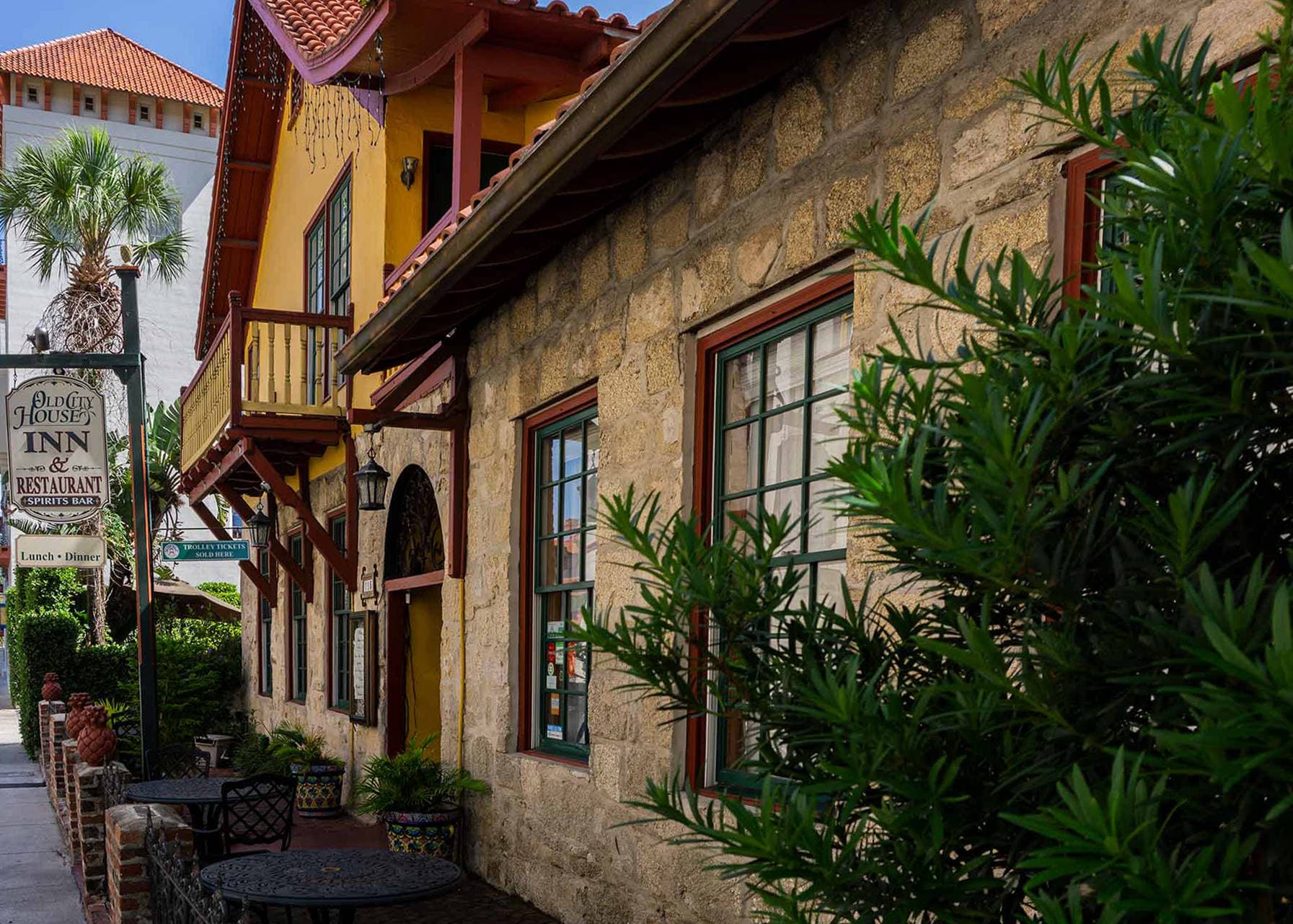 A rustic stone building with green-framed windows, a red tile roof, and an "Old City House Inn & Restaurant" sign is seen from an angle, with lush green plants in the foreground.