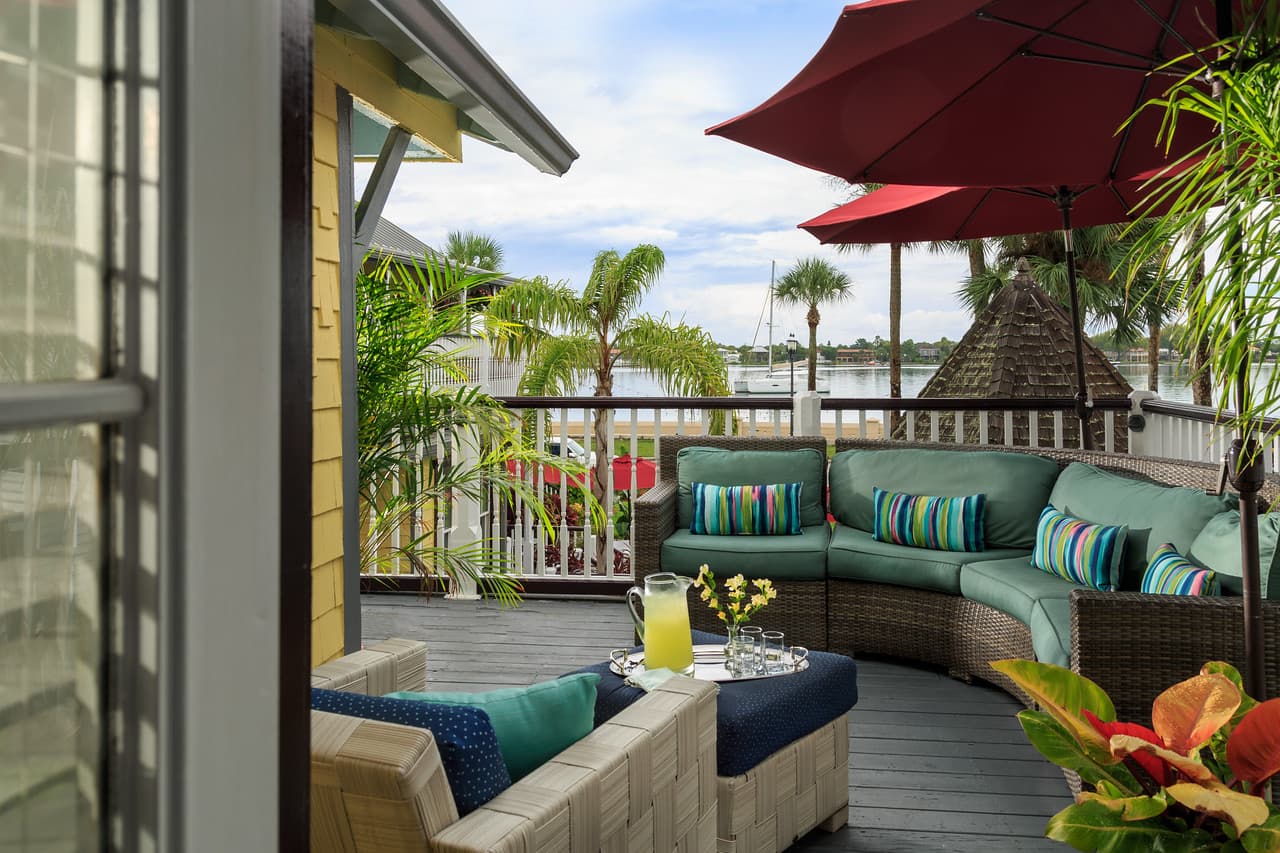 A comfortable outdoor patio with a curved sofa, red umbrellas, and a view of a body of water with boats.