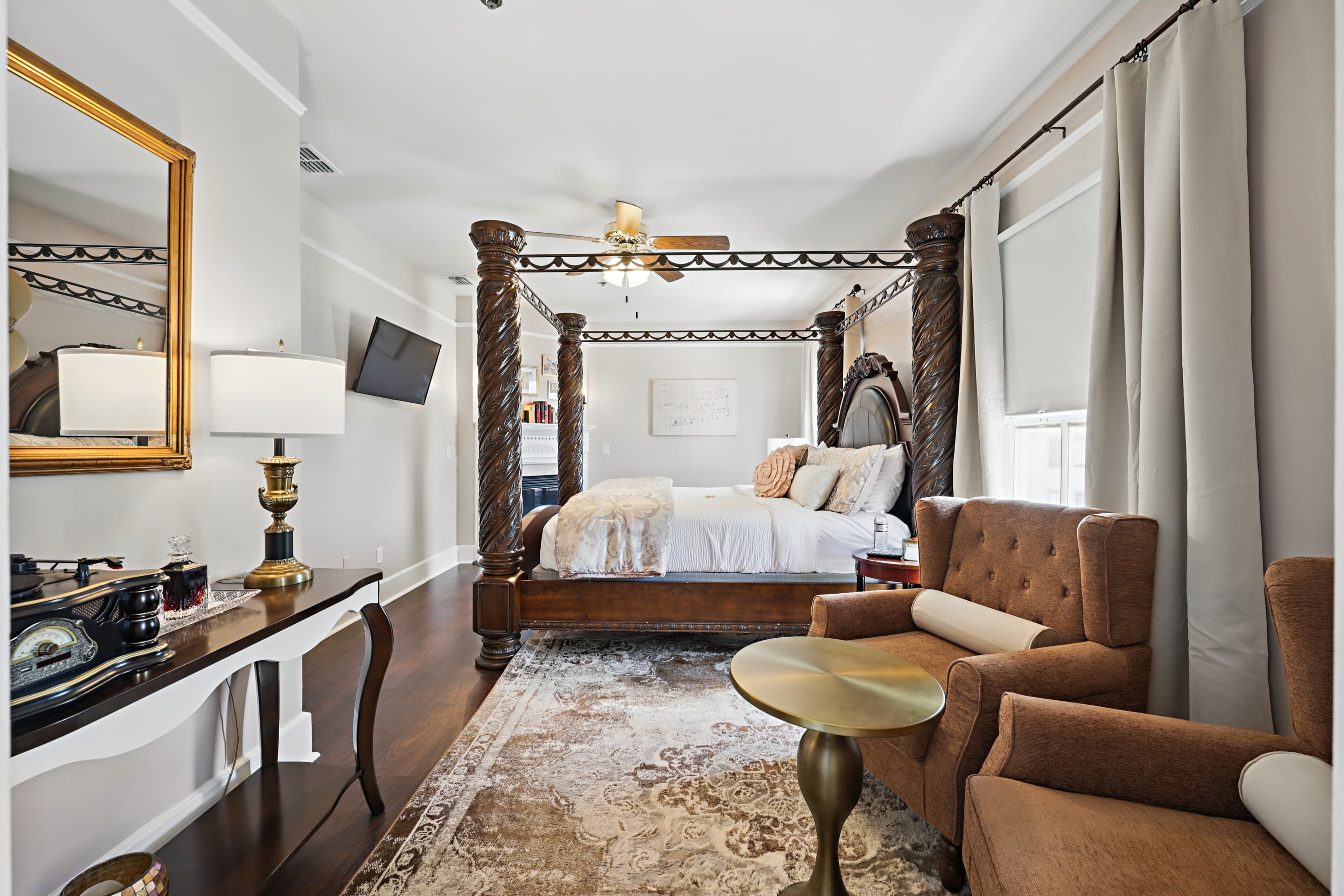 Large guest room with massive 4-poster bed, comfortable chairs, mirror, and an antique phonograph player.