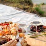 beach picnic with fresh fruit, croissants, bread, and two glasses of white wine, with a bouquet of colorful wildflowers.