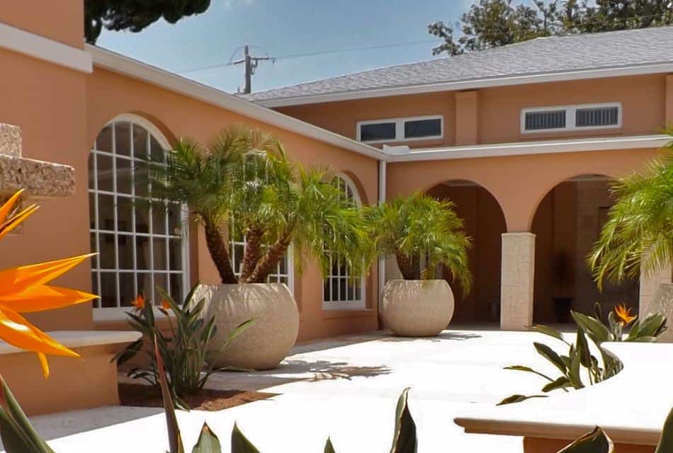 Building with light peach walls, white windows, and large courtyard with plants and flowers