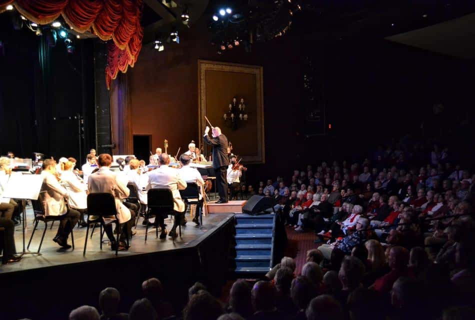 People in an auditorium watching a large orchestra perform on a stage