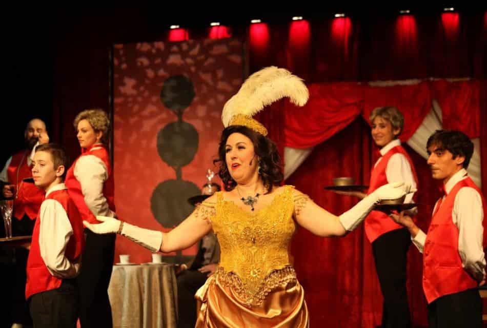 Woman performer in a gold dress and other performers wearing white shirts and red vests on a stage