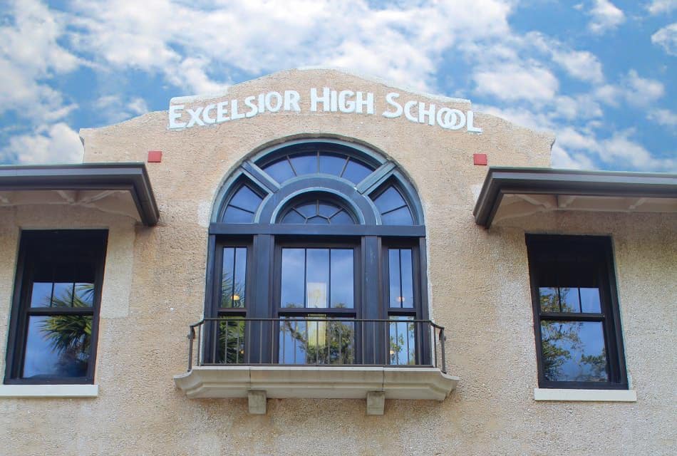 Close up view of a building with light stucco black windows and a sign that says Excelsior High School