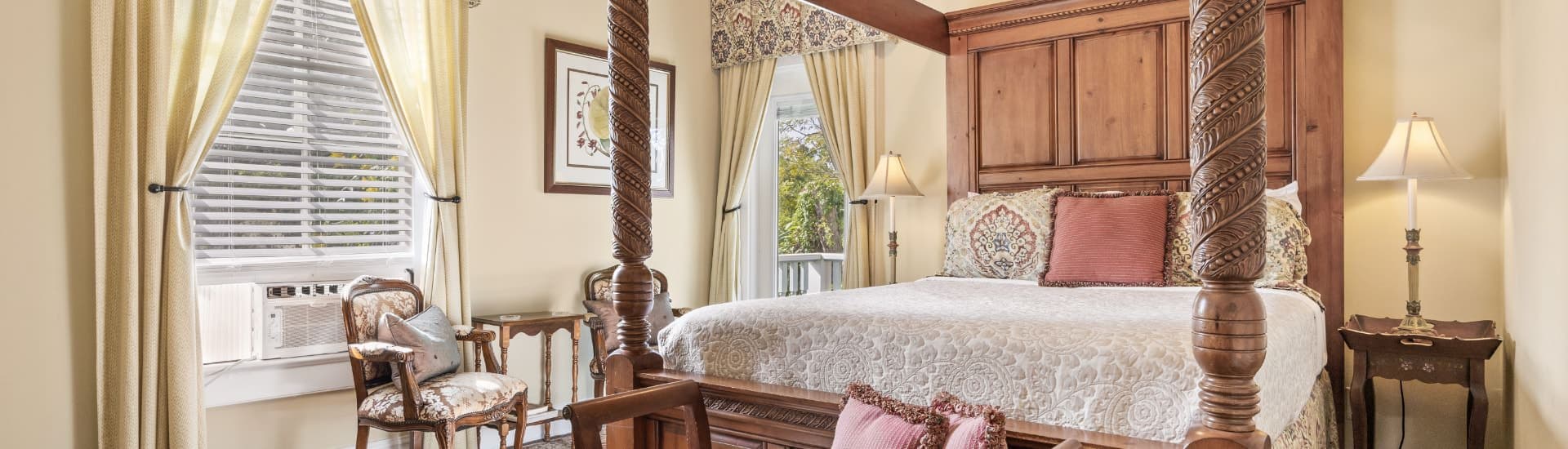 Bedroom with cream walls, white trim, hardwood flooring, large four-poster canopy wooden bed, and sitting area