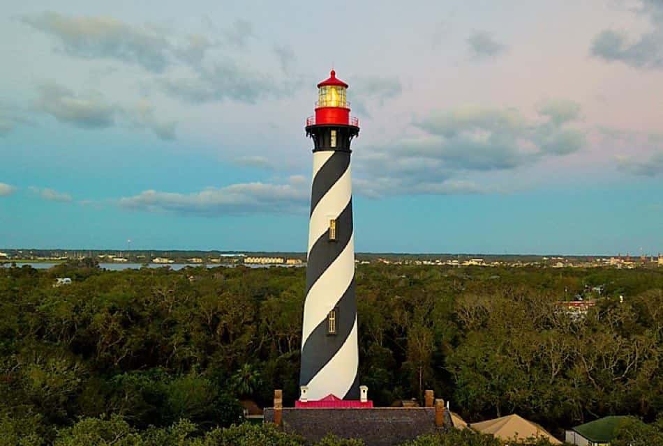 Black and white striped lighthouse with red top surrounded by green trees