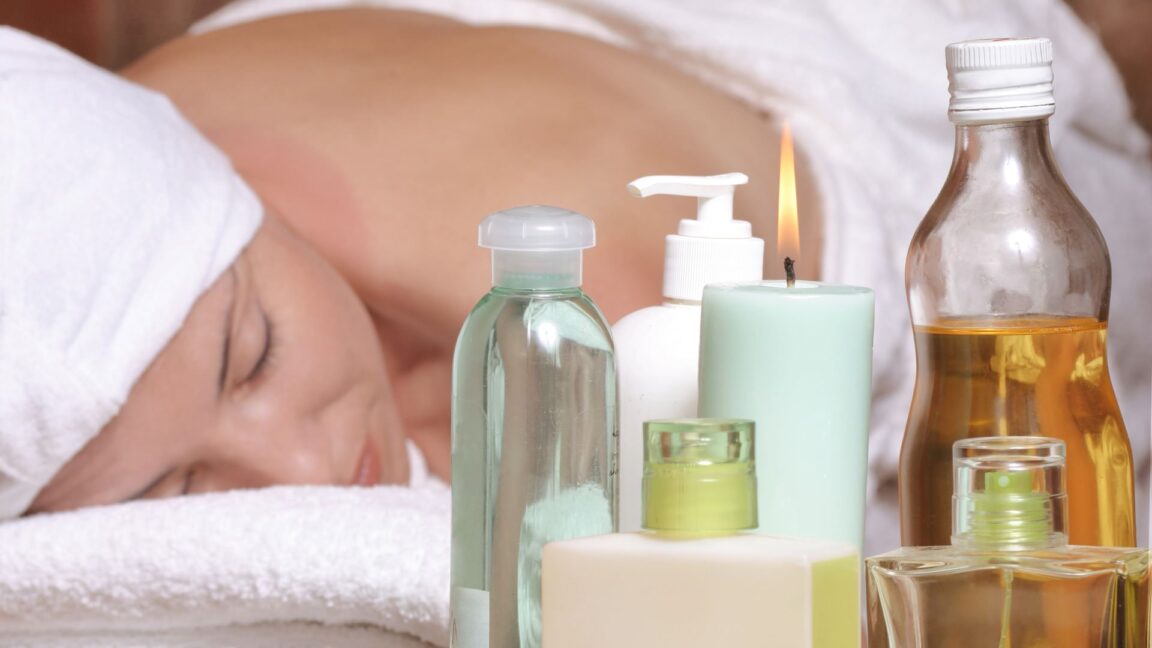 Close up view of woman wrapped in white towel getting a massage with bottles of massage oils and a candle in the foreground