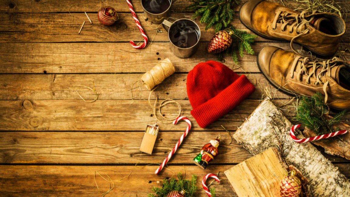 Red stocking cap, old boots, candy canes, ornaments, and evergreen branches on a wood plank background