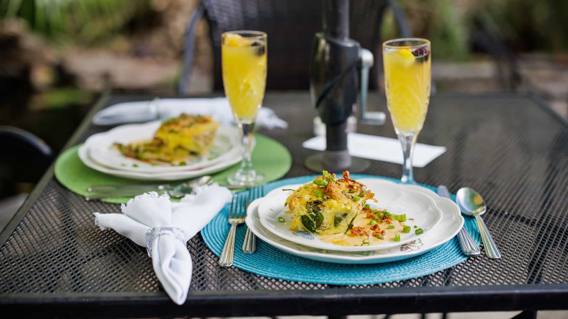 Close up view of two breakfast dishes on white plates on a black metal patio table