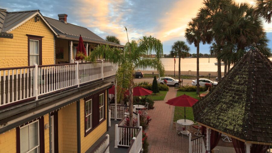 Exterior view of property painted yellow with brown trim, porch on lower and upper levels, gazebo, paver sidewalk, grass, palm trees, and near the water