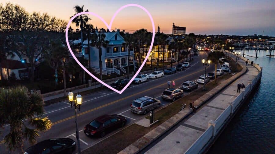 Exterior view of property highlighted with a pink heart around it, porch on lower and upper levels, surrounded by palm trees, and near the water