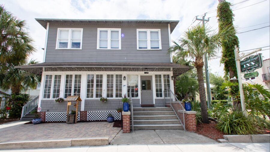 Exterior view of property painted gray with white trim, paver patio, green vegetation, and palm trees