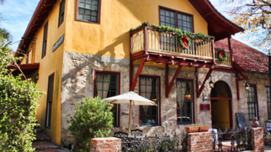 Exterior view of property painted orange with red trim, paver patio, and green vegetation