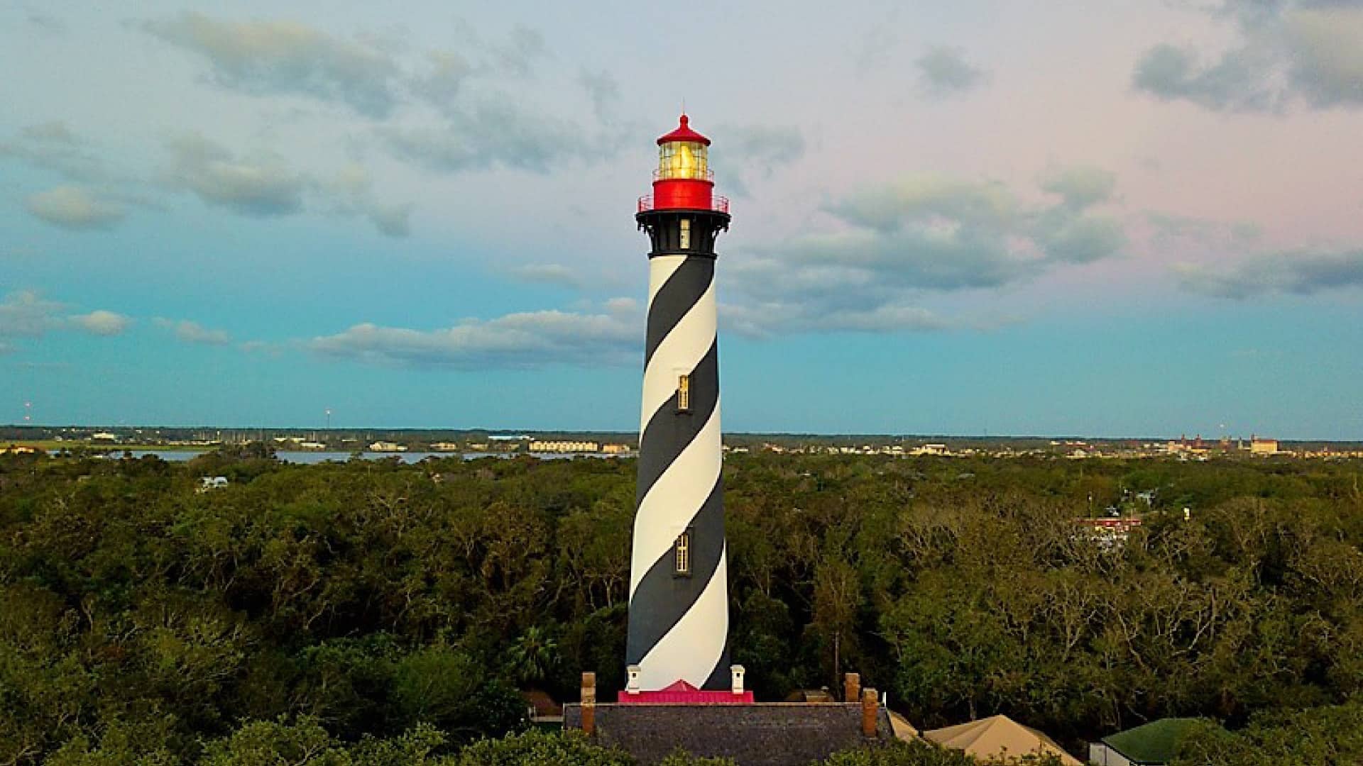 White and black striped lighthouse with red top surrounded by green trees