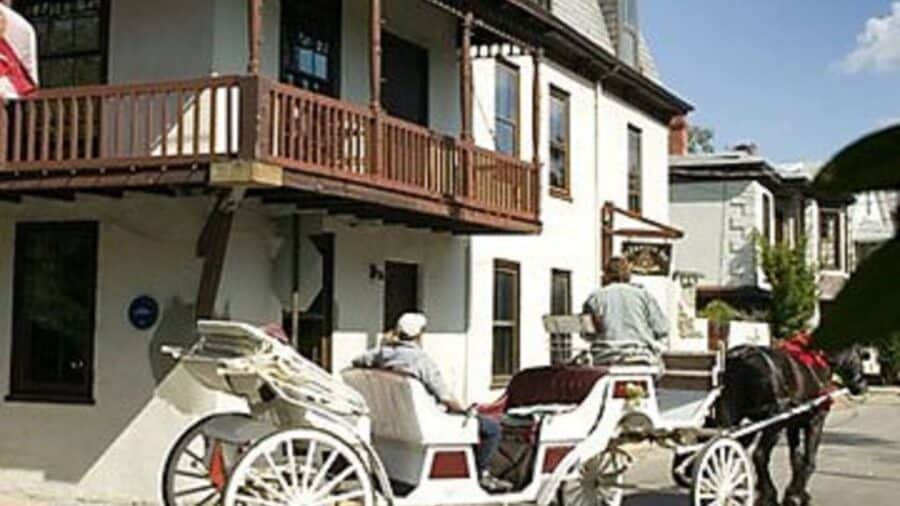 Exterior view of property painted white with brown trim and white horse-drawn carriage moving in front of the property