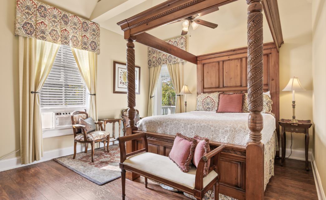 Bedroom with cream walls, white trim, hardwood flooring, large four-poster canopy wooden bed, and sitting area