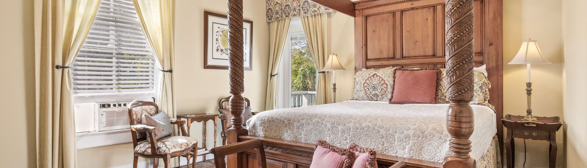 Bedroom with cream walls, white trim, hardwood flooring, large four-poster canopy wooden bed, and sitting area