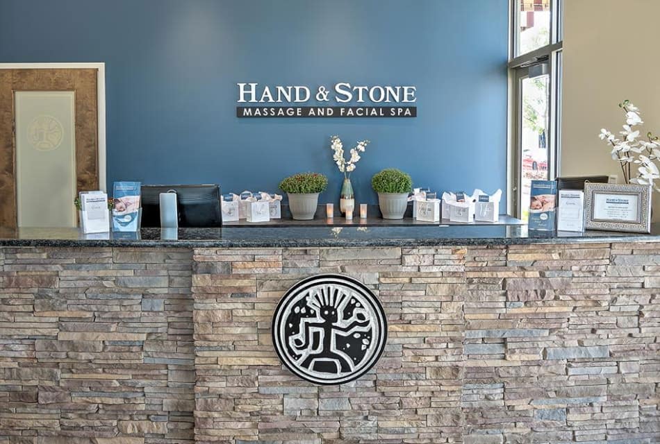Business with blue walls and stone counter with quartz top and the words Hand & Stone Massage and Facial Spa on the wall