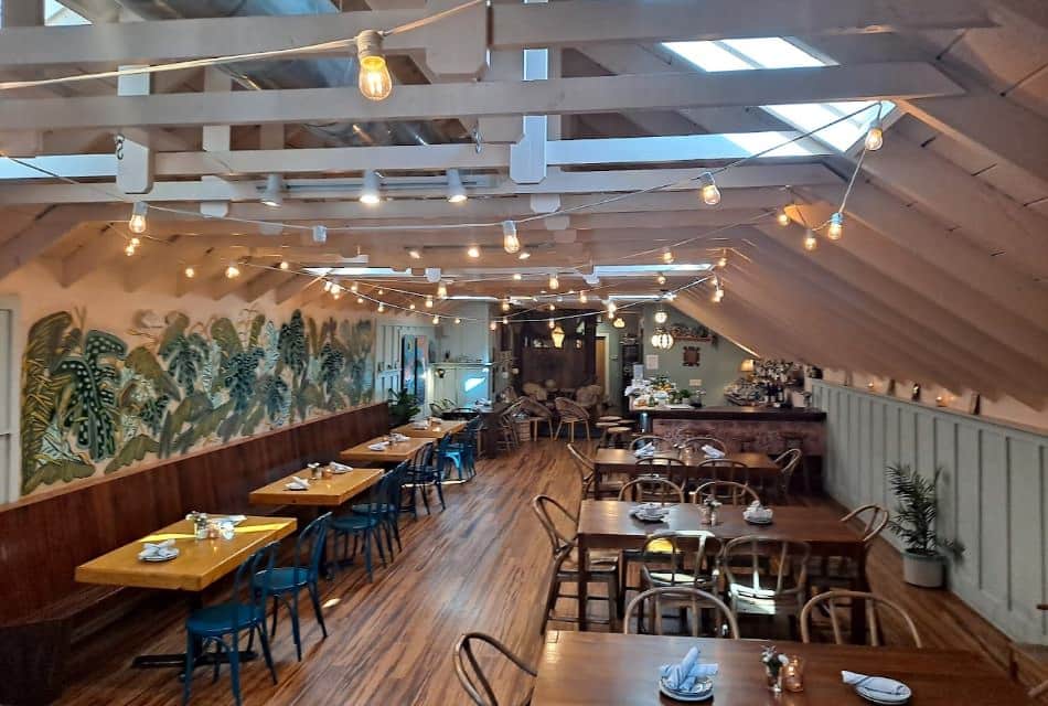 Restaurant dining area with large floral mural, hardwood flooring, wooden tables, and blue and silver metal chairs