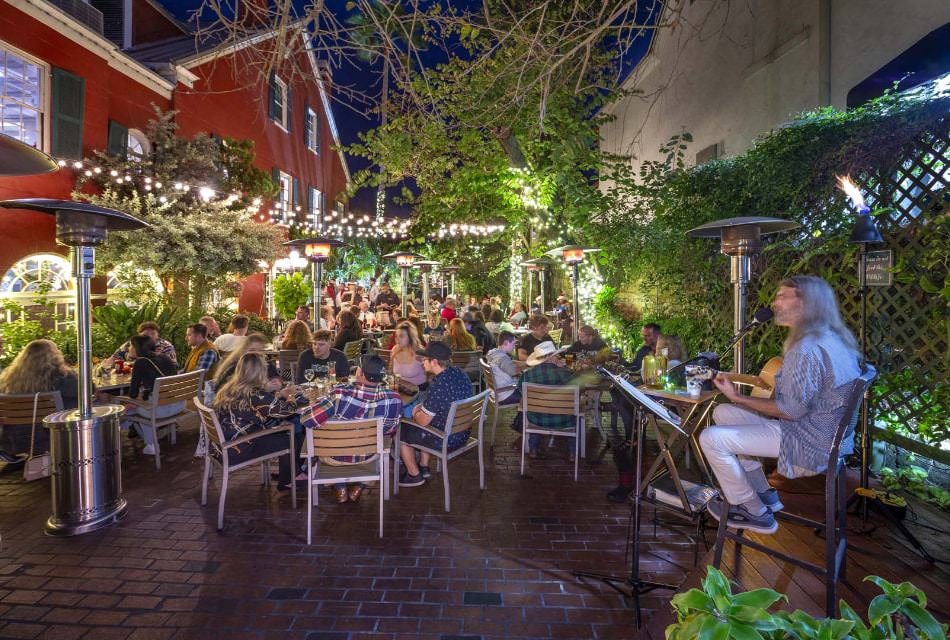 Restaurant's outdoor patio seating at night with lights, tables full of customers, and a man playing a guitar