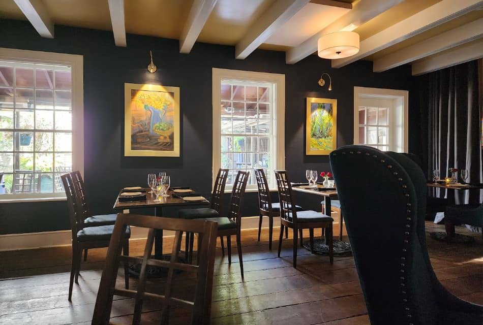 Restaurant dining area with large windows, white trim, green walls, hardwood flooring, wooden tables, and wooden chairs with cushions