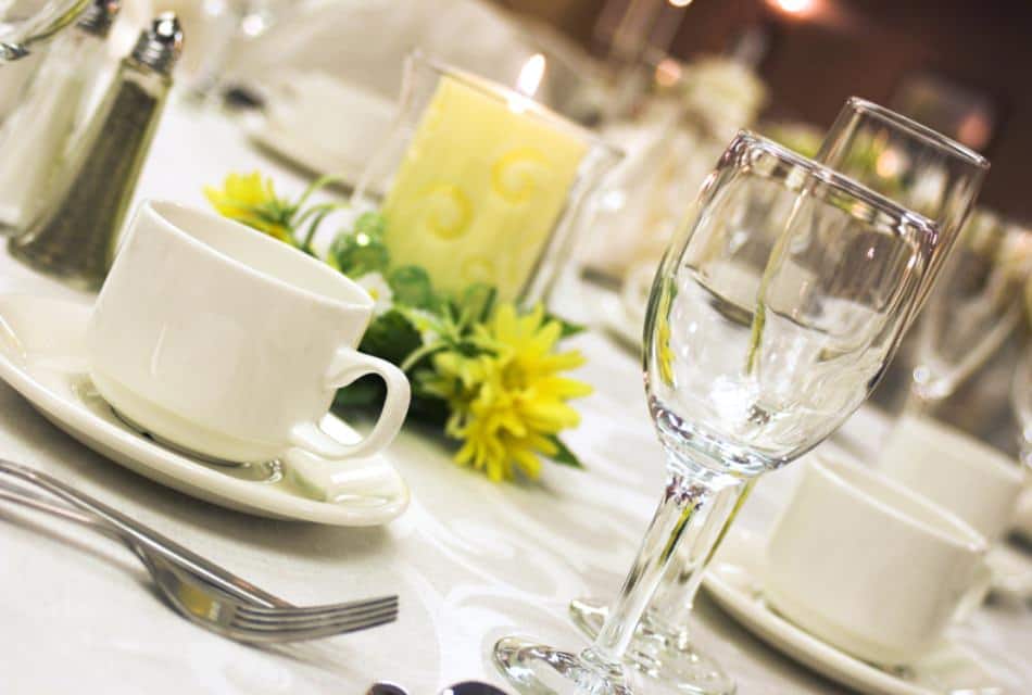 Close up view of white coffee cups, water glasses, and lighted yellow candle on a white tablecloth